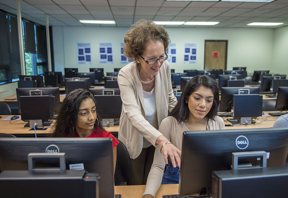 一位图书管理员在罗克维尔图书馆的教室里帮助两名学生使用电脑。