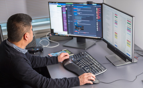 一个男生坐在电脑显示器致力于创建一个视频游戏。
